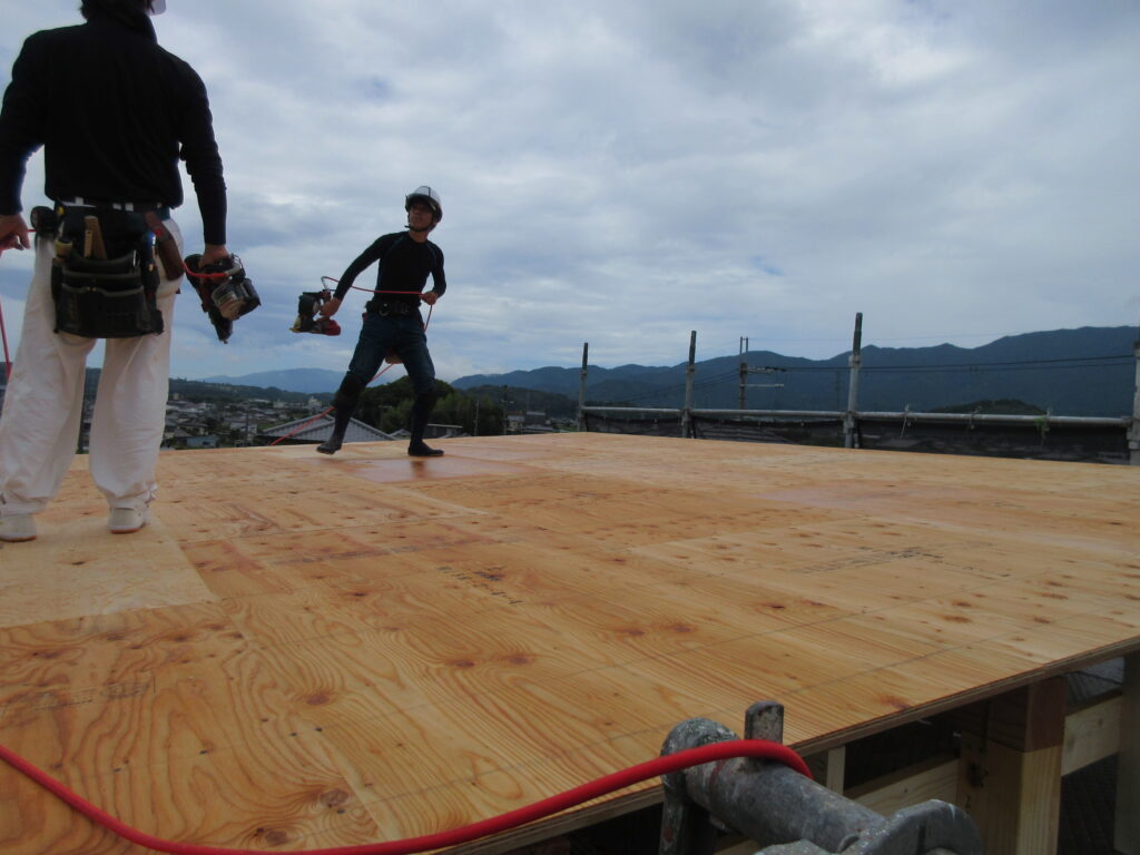 大屋根の板にビスを打っています（曇り空）